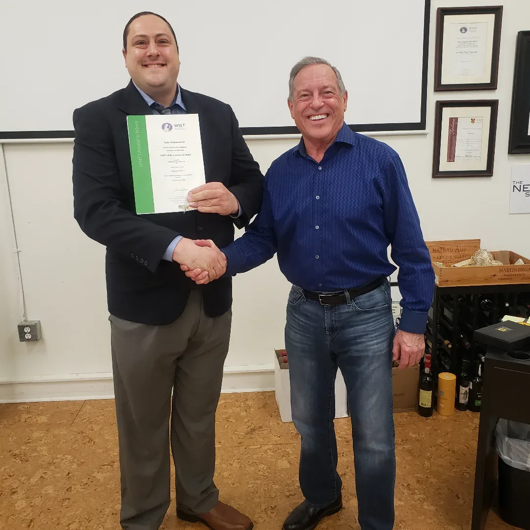 Kyle holding his WSET Level 3 certificate, shaking hands with his instructor